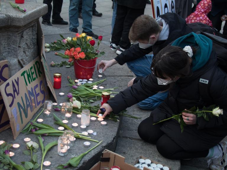 Zwei junge Menschen zünden im Gedenken an die Opfer des rassistischen Anschlags von Hanau Kerzen an und legen Blumen nieder. 
