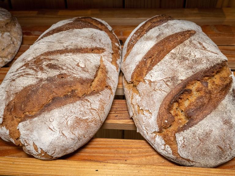 Zwei Brotlaibe liegen nebeneinander in einem Holzregal.