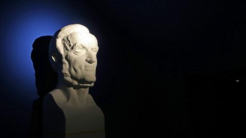 Eine hart angeleuchtete Büste von Richard Wagner vor einem dunkel blauen Hintergrund.