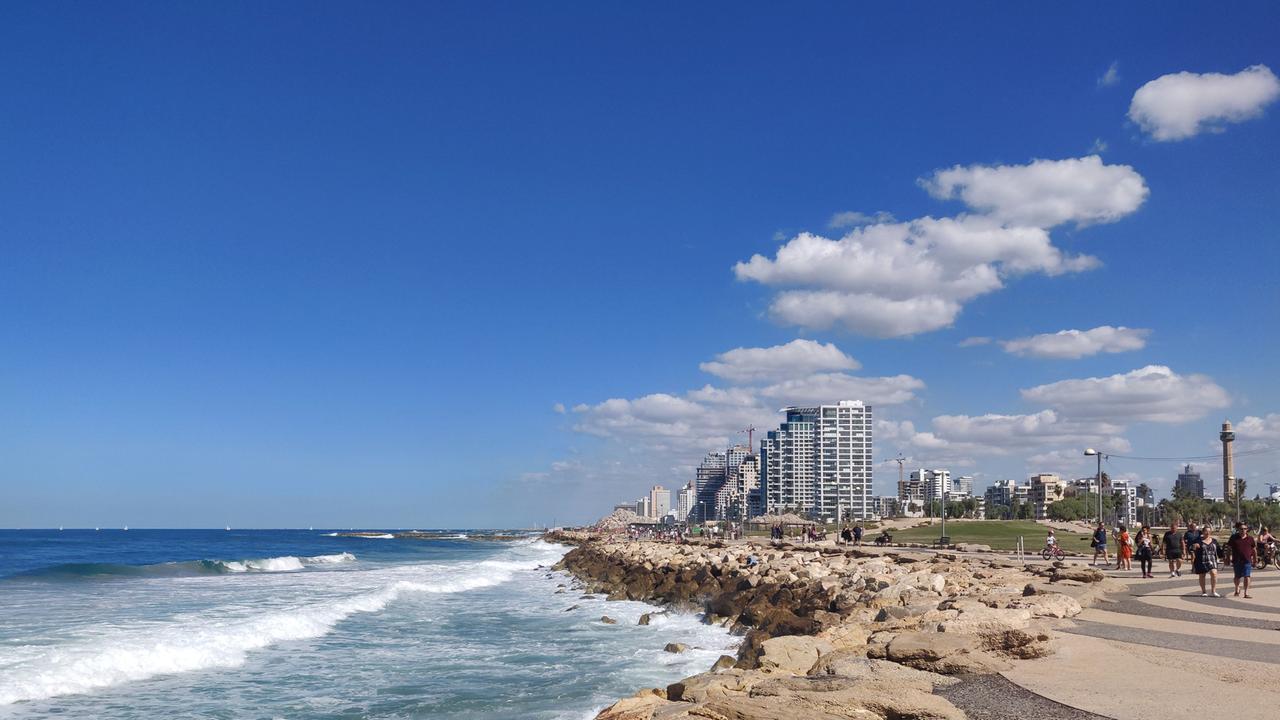 Malerische Aussicht auf die Küste von Tel Aviv mit klarem blauen Himmel, felsiger Küste und modernen Gebäuden im Hintergrund. 