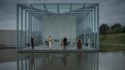 Die vier Musiker des Quartetts stehen in einer Art Glashalle, die zum Wasser hin komplett offen ist und sich im Wasser spiegelt.