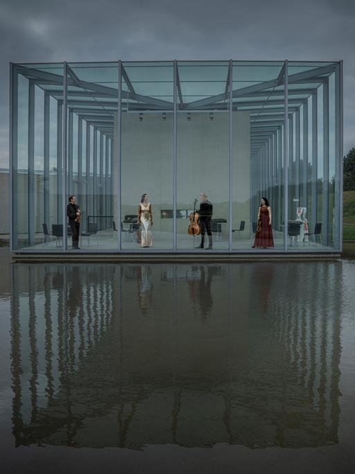 Die vier Musiker des Quartetts stehen in einer Art Glashalle, die zum Wasser hin komplett offen ist und sich im Wasser spiegelt.