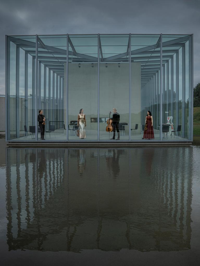 Die vier Musiker des Quartetts stehen in einer Art Glashalle, die zum Wasser hin komplett offen ist und sich im Wasser spiegelt.