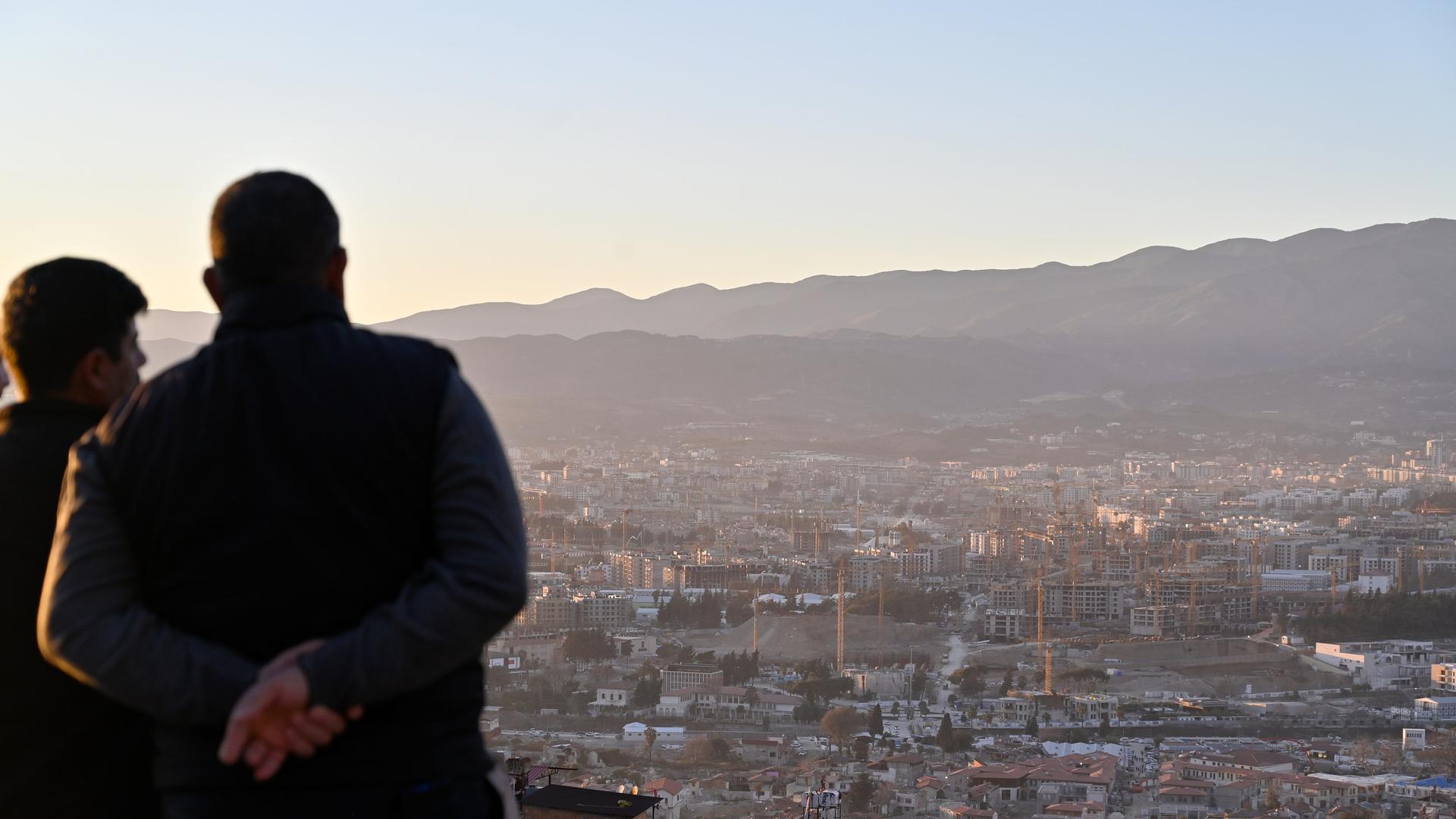 Zwei Männer blicken von einer Erhöhung auf die Stadt und ihre zahlreichen Baustellen, zwei Jahre nach den verheerenden Erdbeben in der Türkei. Zwei Männer blicken von einer Erhöhung auf die Stadt und ihre zahlreichen Baustellen, zwei Jahre nach den verheerenden Erdbeben in der Türkei.