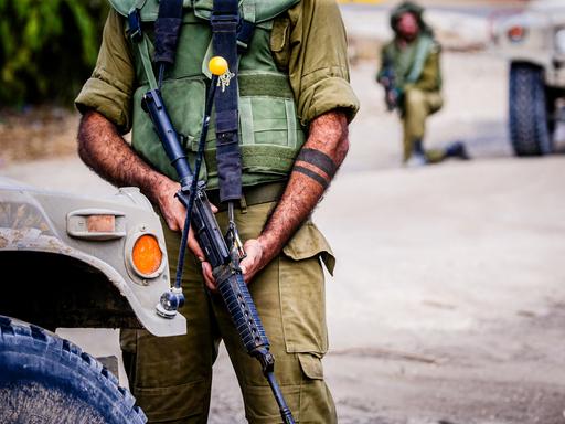 Ein mit einem schweren Gewehr bewaffneter israelischer Soldat. Sein Gesicht ist nicht zu sehen.
