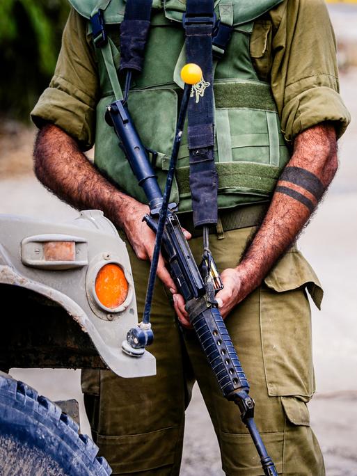 Ein mit einem schweren Gewehr bewaffneter israelischer Soldat. Sein Gesicht ist nicht zu sehen.