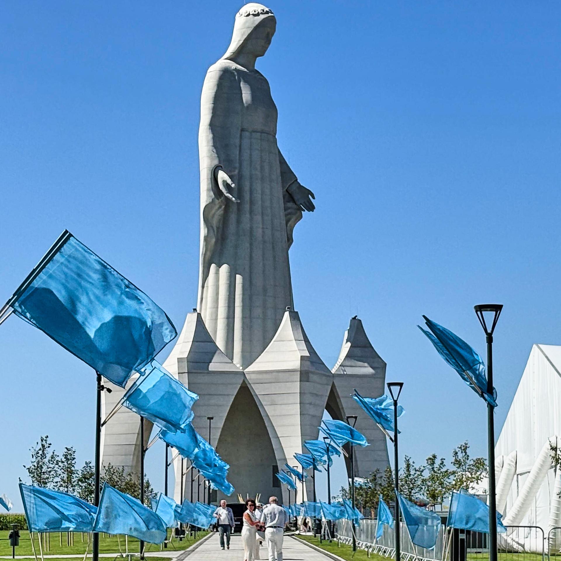 Auf dem Weg zu der riesigen Statue stehen unzählige blaue Fahnen. Darüber ein stahlblauer wolkenloser Himmel.  