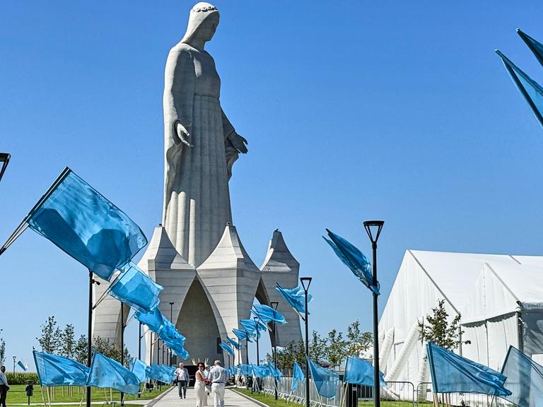Auf dem Weg zu der riesigen Statue stehen unzählige blaue Fahnen. Darüber ein stahlblauer wolkenloser Himmel. Auf dem Weg zu der riesigen Statue stehen unzählige blaue Fahnen. Darüber ein stahlblauer wolkenloser Himmel.