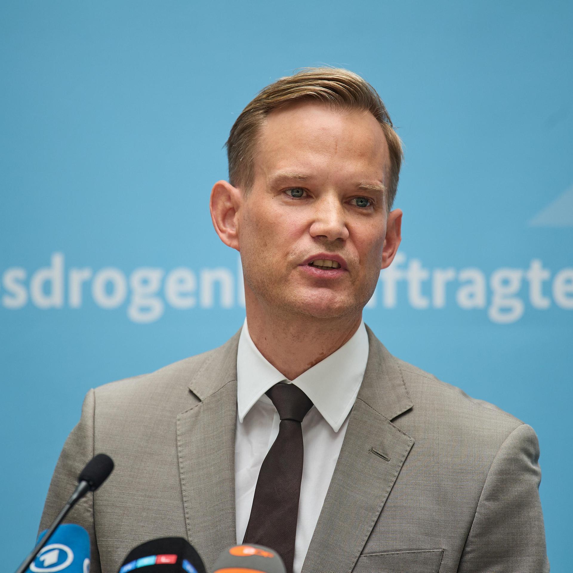 Hendrik Streeck steht vor einer blauen Wand mit der Aufschrift "bundesdrogenbeauftragter.de".