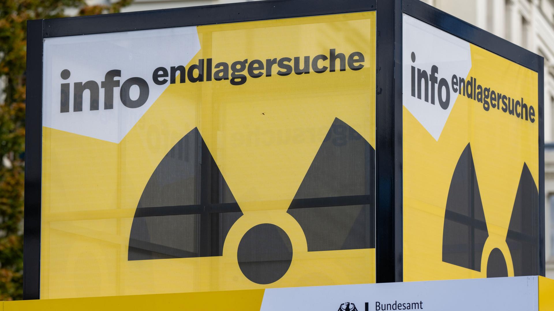 Zu sehen ist ein Infostandstand in Würfelform. Auf den Seiten ist das Zeichen für Radioaktivität abgebildet. Darüber steht geschrieben: „Info Endlagersuche“. 