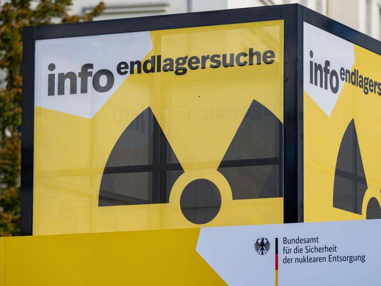 Zu sehen ist ein Infostandstand in Würfelform. Auf den Seiten ist das Zeichen für Radioaktivität abgebildet. Darüber steht geschrieben: „Info Endlagersuche“. 