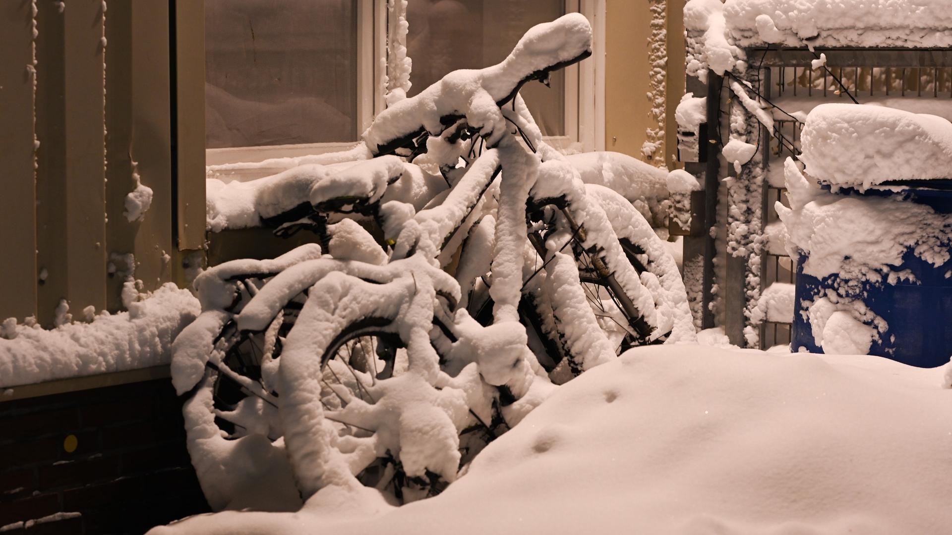Eingeschneite Fahrräder stehen an einer Hauswand.