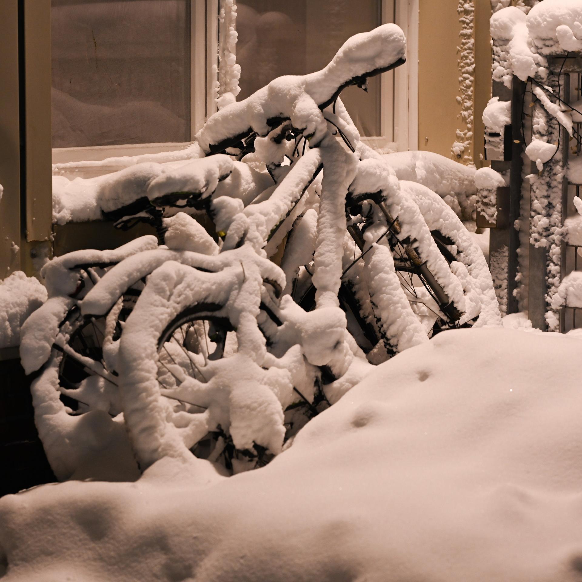Eingeschneite Fahrräder stehen an einer Hauswand.