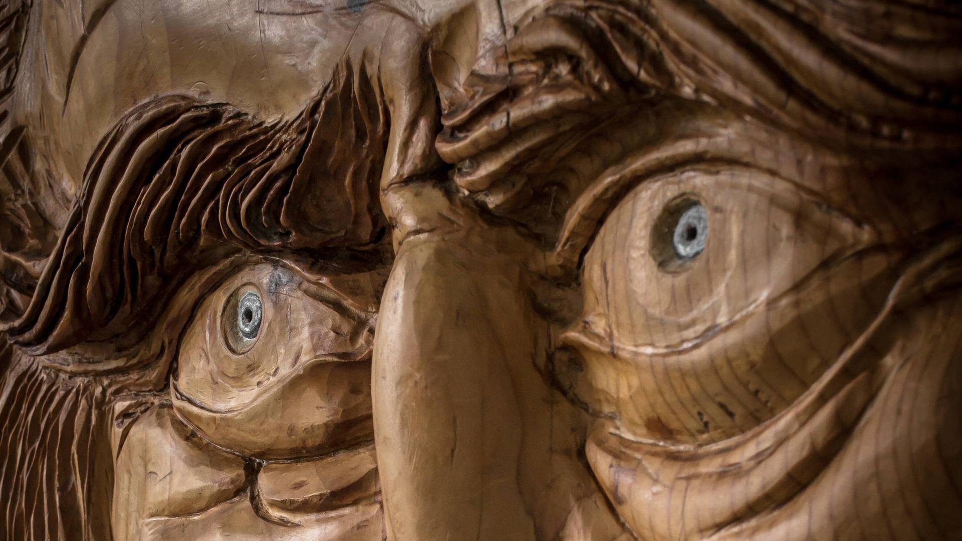 Foto einer Holzarbeit, die das Gesicht mit markanten Augen und Augenbrauen eines alten Mannes zeigt.