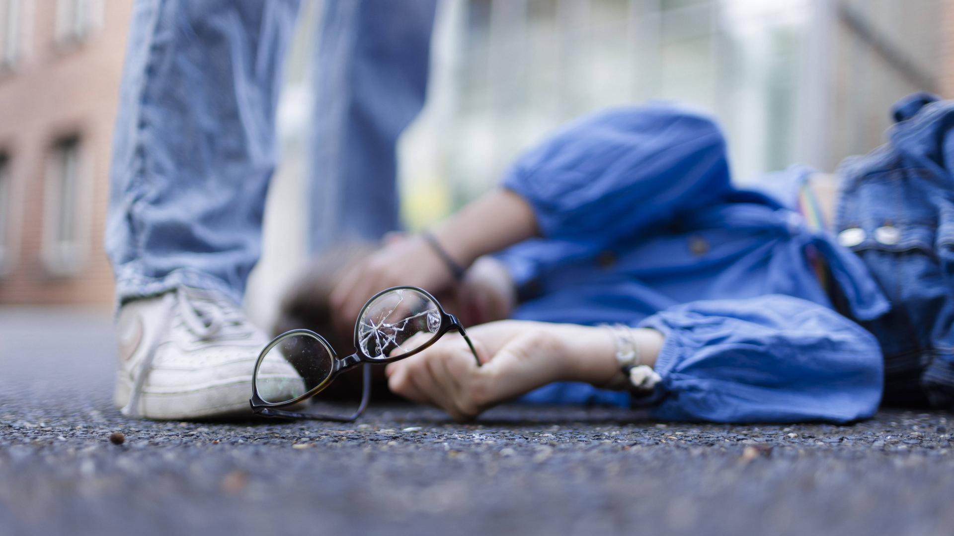 Ein Junge liegt mit einer zerbrochenen Brille auf dem Boden und hält sich die Hand vor das Gesicht (Symbolbild)
