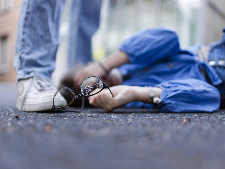 Ein Junge liegt mit einer zerbrochenen Brille auf dem Boden und hält sich die Hand vor das Gesicht (Symbolbild)