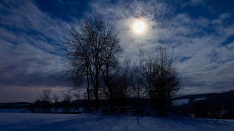 Nachthimmel mit Mond, der durch einen Baum in verschneiter Landschaft scheint