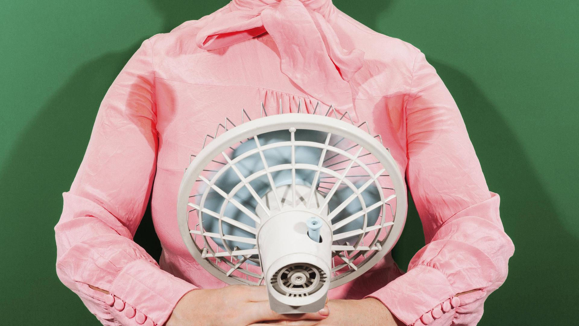 Eine Geschäftsfrau mit verschwitzten Achselhöhlen, die vor einem Ventilator steht.