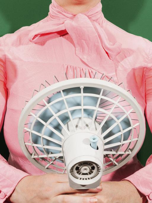 Eine Geschäftsfrau mit verschwitzten Achselhöhlen, die vor einem Ventilator steht.