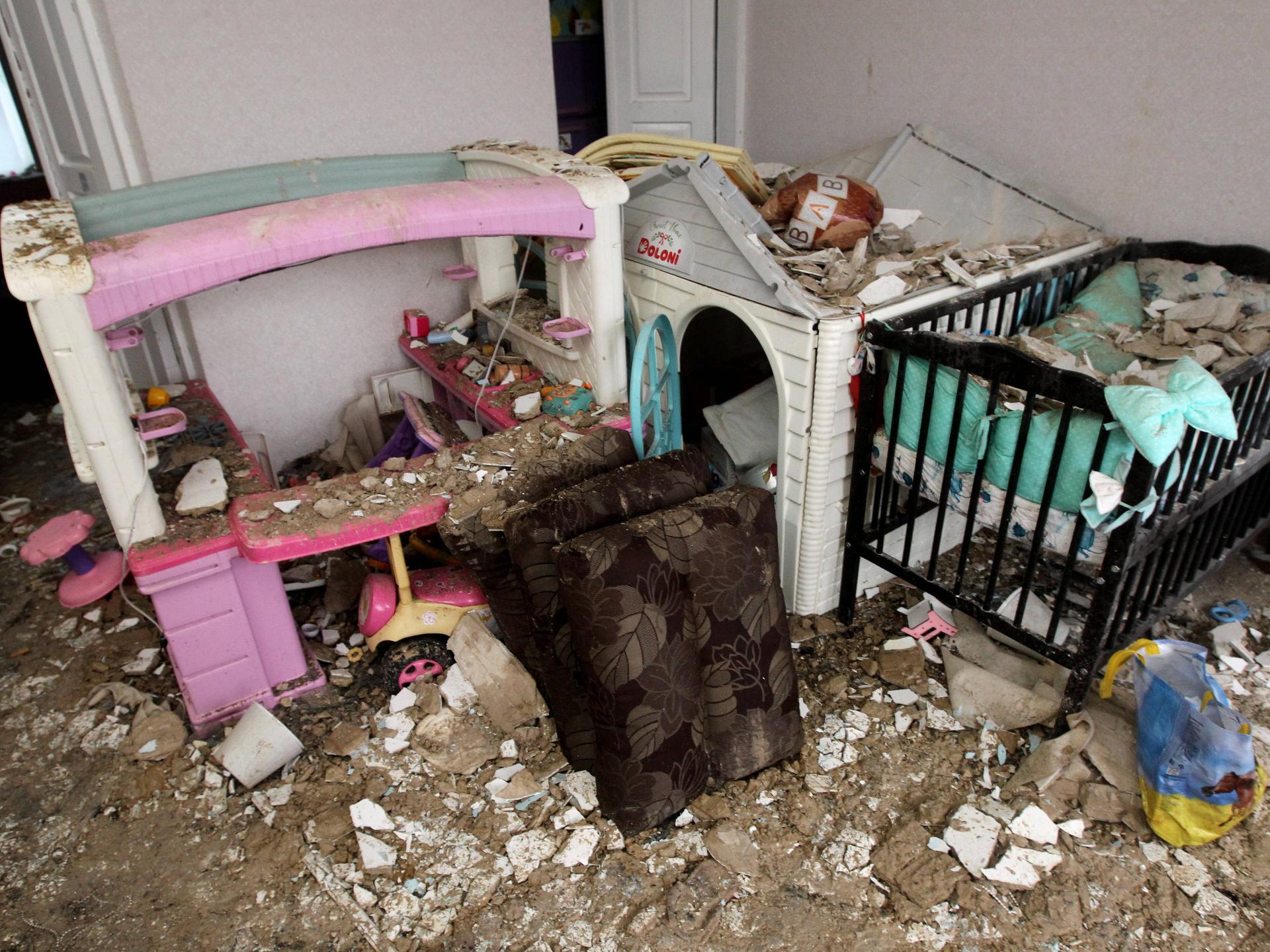 Man sieht ein Kinderzimmer mit einem Gitterbett und einem Puppenhaus, drumherum viel Schutt. Aufgenommen wurde das Foto am 12. Februar 2026 in Dnipro (Ukraine), nachdem das Wohngebäude von einer russischen Drohne getroffen wurde.
