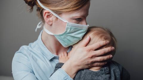 Eine Mutter mit medizinischer Maske trägt ihr krankes Kleinkind auf dem Arm.