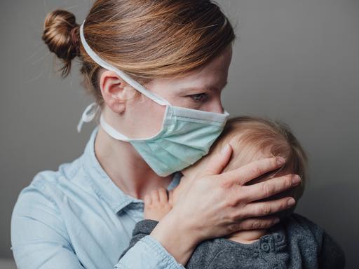 Eine Mutter mit medizinischer Maske trägt ihr krankes Kleinkind auf dem Arm.