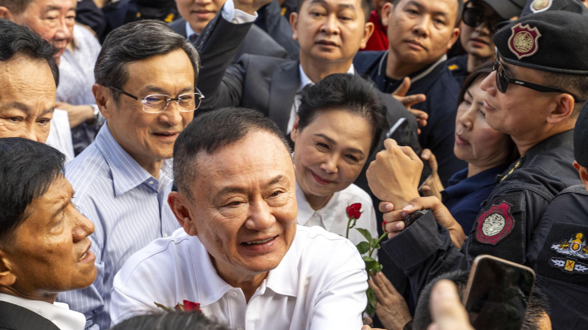 Der ehemalige thailändische Premierminister Thaksin Shinawatra lächelt, während er Unterstützer begrüßt, die um ihn herum stehen. 