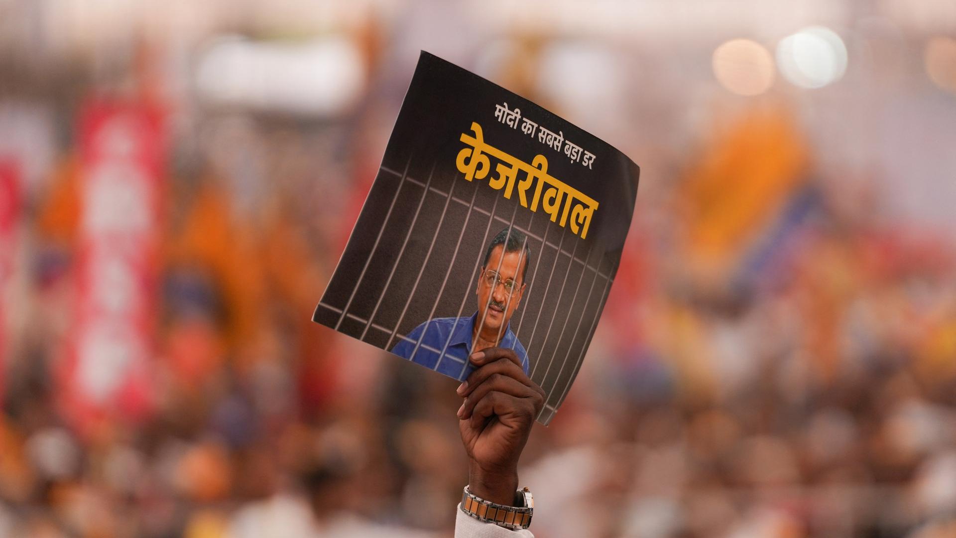 Opposition in Indien protestiert gegen Festnahme des Regional-Regierungschefs Kejriwal der Metropolregion Delhi. Im Bild-Vordergrund wird ein Plakat in die Höhe gehalten, das ihn hinter Gittern zeigt.