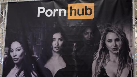 Bei einer Messe ist am Stand von Pornhub das Firmenlogo auf einem Plakat mit vier Frauen in Reizwäsche zu sehen.
