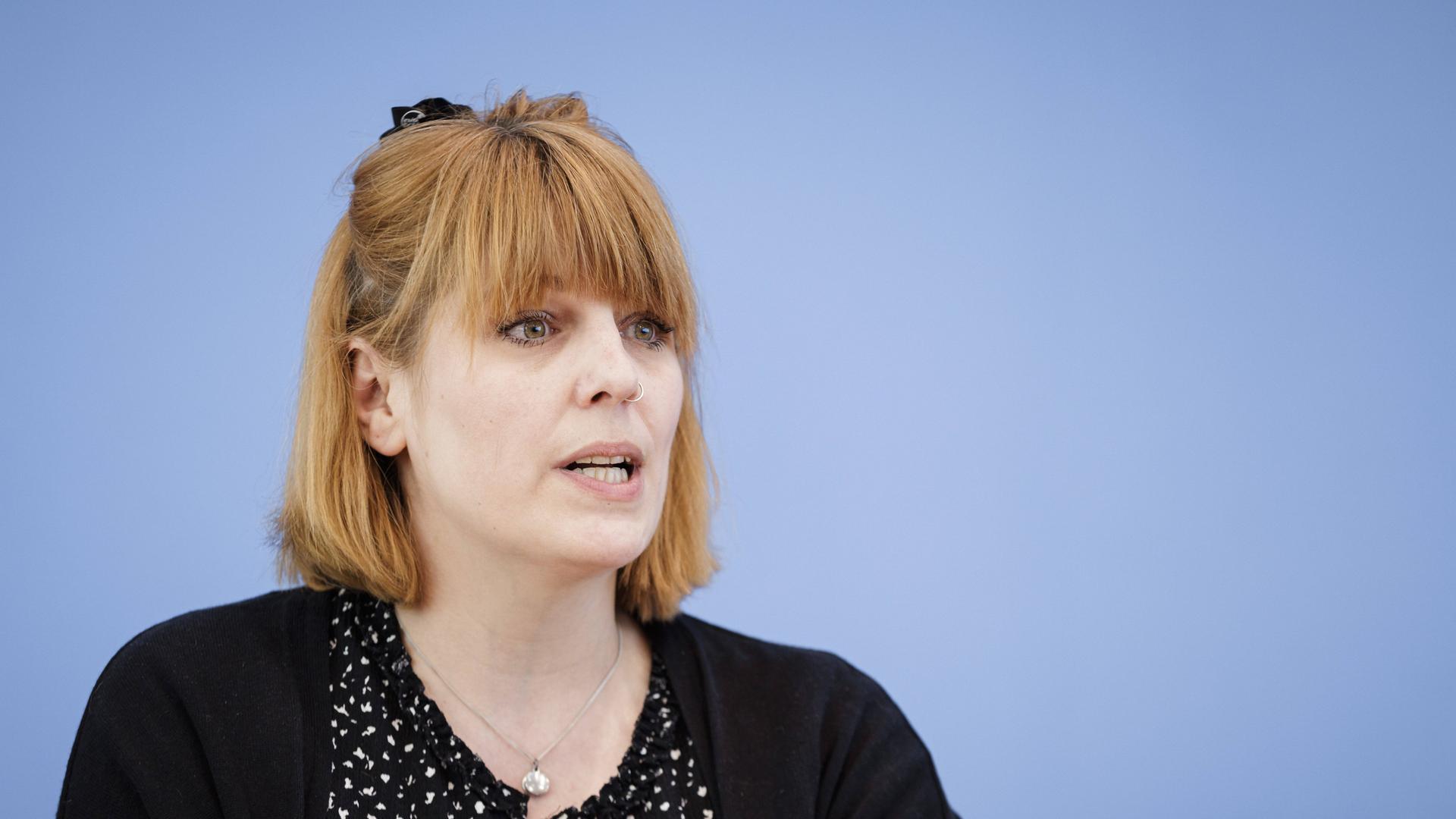 Die Sozialpsychologin Pia Lamberty sitzt bei einer Pressekonferenz vor einer blauen Wand