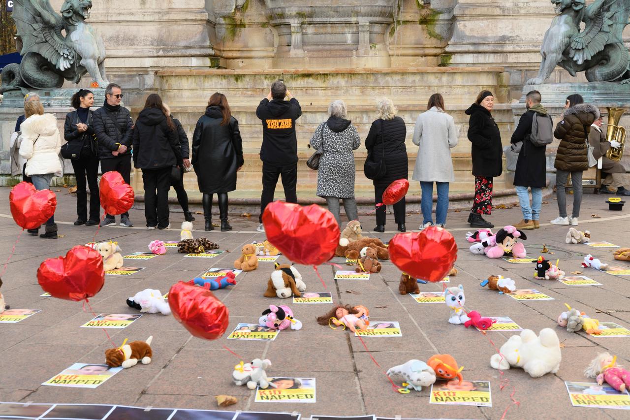 Menschen stehen in Paris vor einem Monument, in ihrem Rücken haben sie die auf dem Boden liegenden Bilder der entführten Geiseln mit Stofftieren und Luftballons geschmückt.