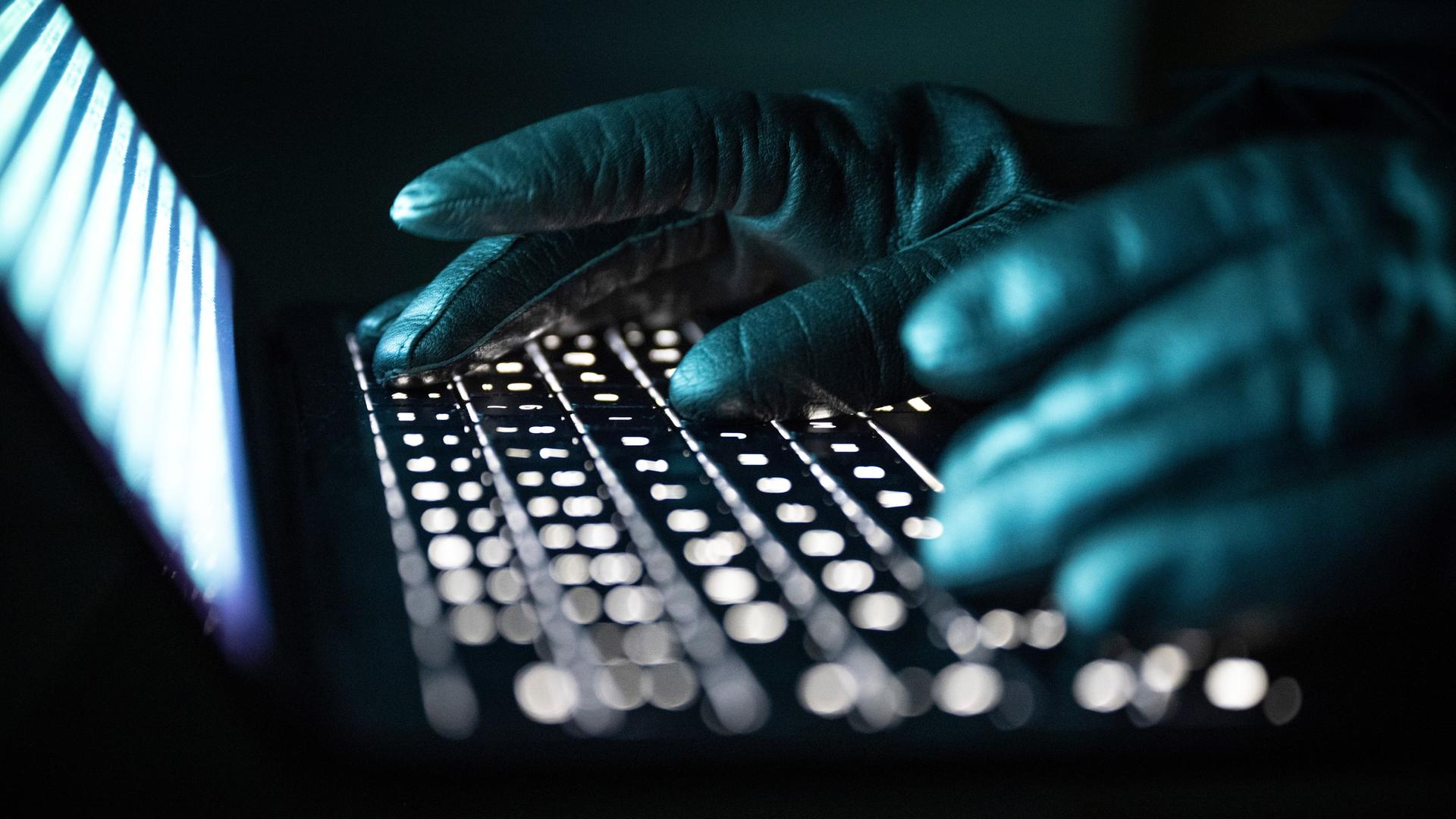 Eine Person mit schwarzen handschuhen tippt auf einer beleuchteten Laptop-Tastatur. (Gestellte Szene)