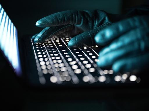 Eine Person mit schwarzen handschuhen tippt auf einer beleuchteten Laptop-Tastatur. (Gestellte Szene) Eine Person mit schwarzen handschuhen tippt auf einer beleuchteten Laptop-Tastatur. (Gestellte Szene)