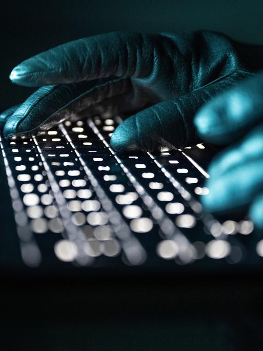 Eine Person mit schwarzen Handschuhen tippt auf einer beleuchteten Laptop-Tastatur. (Gestellte Szene) Eine Person mit schwarzen Handschuhen tippt auf einer beleuchteten Laptop-Tastatur. (Gestellte Szene)