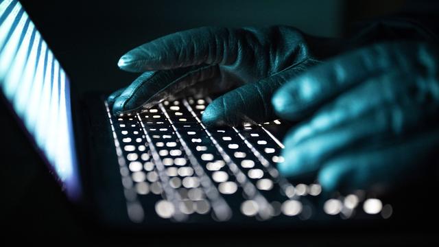 Eine Person mit schwarzen handschuhen tippt auf einer beleuchteten Laptop-Tastatur. (Gestellte Szene)