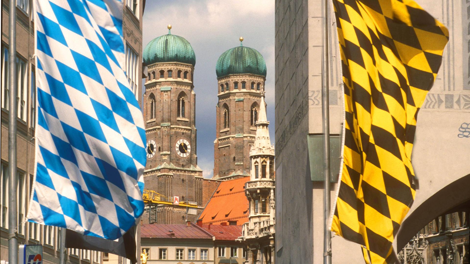 Türme der Frauenkirche in München mit weiß-blauen Flaggen im Vordergrund.