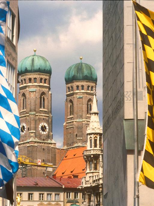 Türme der Frauenkirche in München mit weiß-blauen Flaggen im Vordergrund.