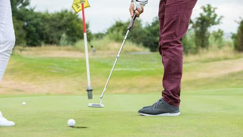 Ein Golfspieler locht auf einem Golfplatz in Köln den Golfball ein.