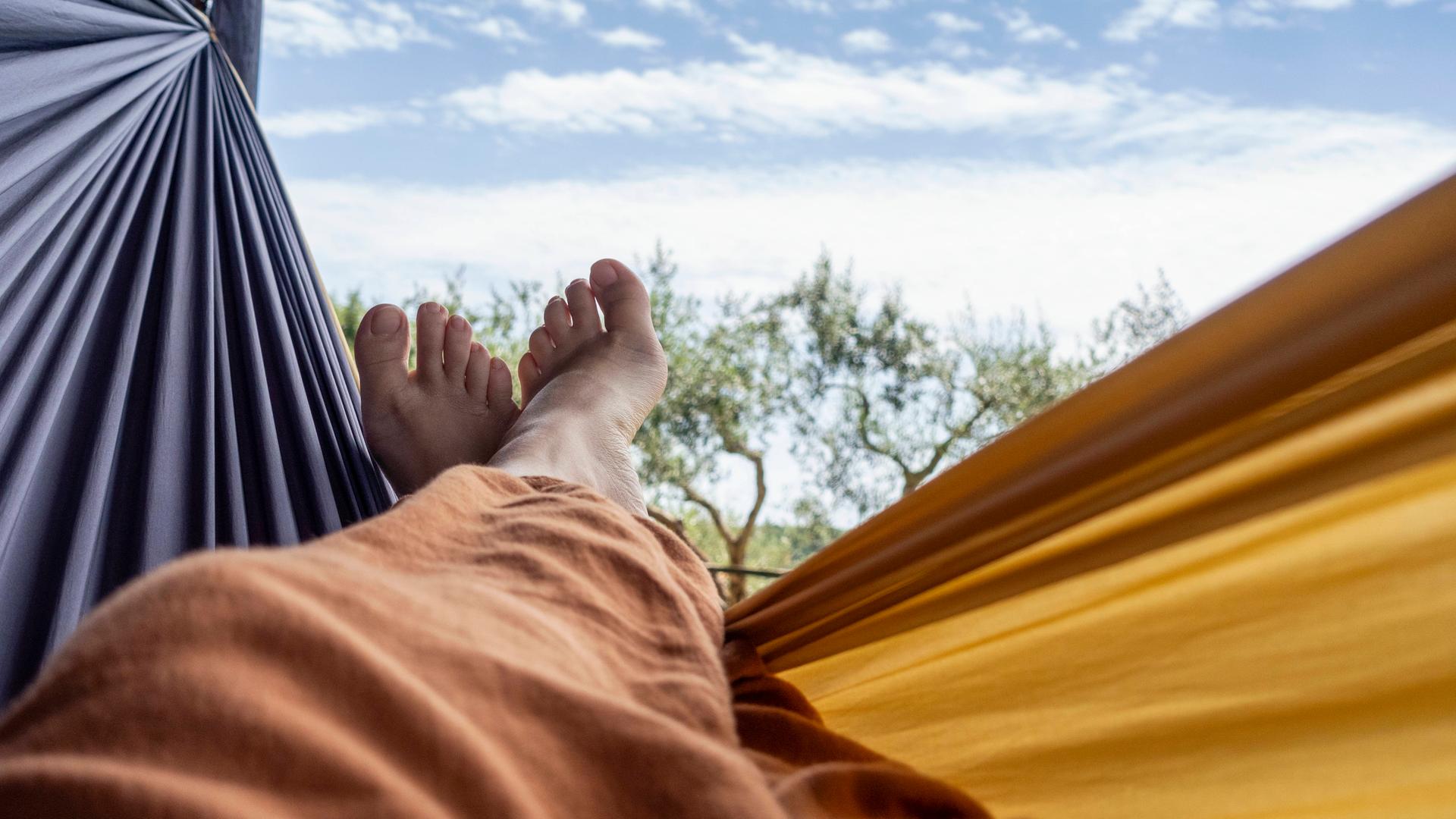 Übereinandergeschlagene nackte Füße in einer Hängematte vor blauem Himmel