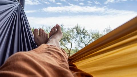 Übereinandergeschlagene nackte Füße in einer Hängematte vor blauem Himmel