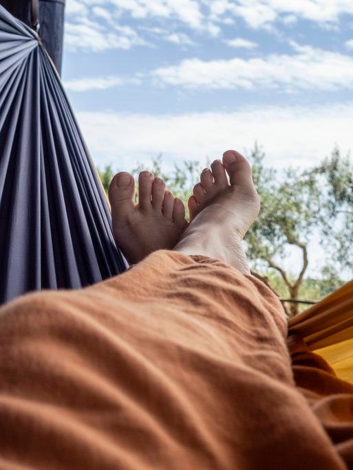 Übereinandergeschlagene nackte Füße in einer Hängematte vor blauem Himmel Übereinandergeschlagene nackte Füße in einer Hängematte vor blauem Himmel