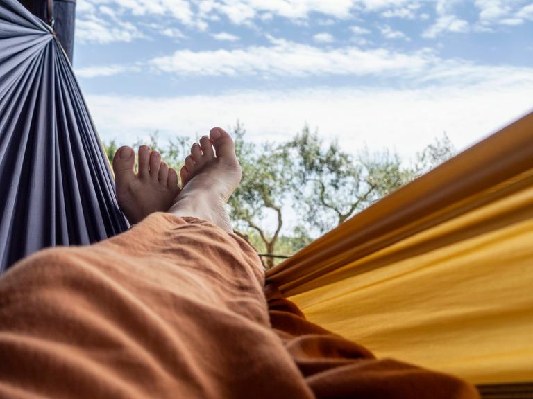 Übereinandergeschlagene nackte Füße in einer Hängematte vor blauem Himmel