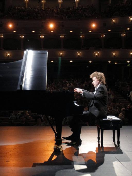 Ein Mann mit kurzen Locken sitzt an einem schwarzen Flügel. Er gibt gerade ein Konzert. Er hat 2013 am Van Cliburn Wettbewerb in den USA teilgenommen.