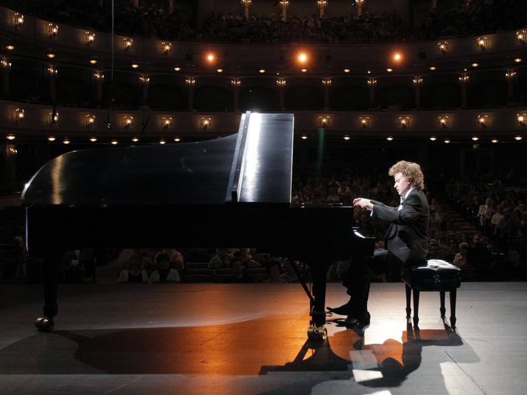 Ein Mann mit kurzen Locken sitzt an einem schwarzen Flügel. Er gibt gerade ein Konzert. Er hat 2013 am Van Cliburn Wettbewerb in den USA teilgenommen.