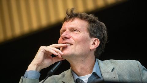 Hartmut Rosa steht an einem Mikrofon und hält die Hand an sein Kinn