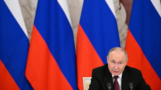 Russlands Präsident Wladimir Putin sitzt vor mehreren russischen Flaggen und spricht in ein Mikrofon.