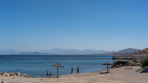 Ein Strand in Ceuta, im Hintergrund der Grenzzaun und eine Barriere im Meer