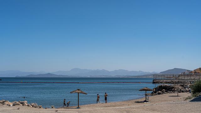 Am Strand von Ceuta baden ein paar Menschen, das Meer ist ruhig und wird von einer Grenzbarriere durchzogen, die  sich am Festland mit einem Zaun fortsetzt.