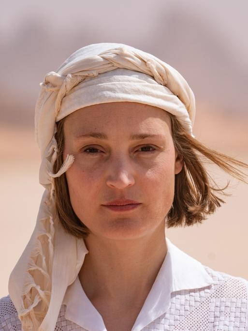 Eine Frau mit weißer Kopfbedeckung und weißem Hemd in der Wüste.