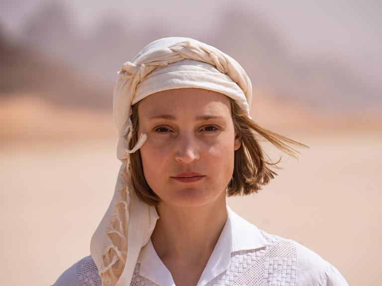 Eine Frau mit weißer Kopfbedeckung und weißem Hemd in der Wüste.